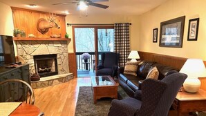 A cozy living room with a stone fireplace, a leather sofa, a dining table, and a television.