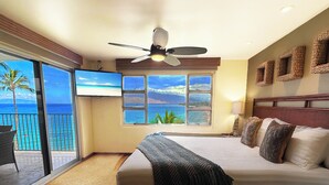 Ein Hotelzimmer mit Bett, Deckenventilator, Fernseher, Fenster mit Meerblick und Balkon mit einem Stuhl.