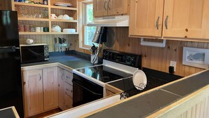 A kitchen with wooden cabinets, a black refrigerator, a microwave, a stove, and a sink. - Cozy, lakeside cottage for your family vacation (Woodstock)