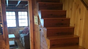 A wooden staircase leading to a loft bedroom with a window and a small table. - Cozy, lakeside cottage for your family vacation (Woodstock)