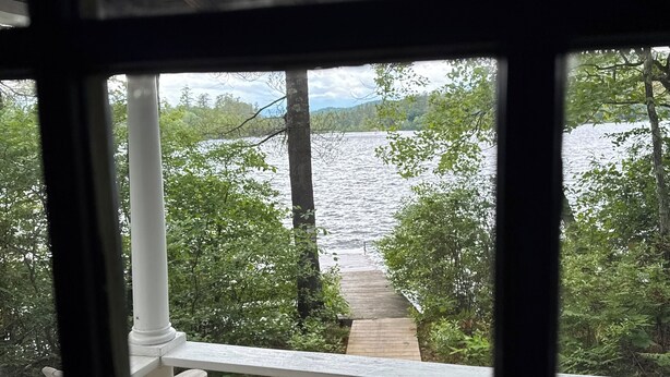 A wooden deck with two Adirondack chairs overlooking a body of water and a forested area. - Cozy, lakeside cottage for your family vacation (Woodstock)