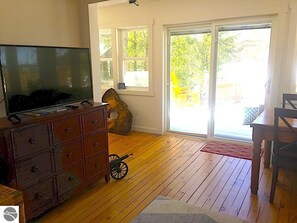 Una stanza con pavimento in legno, una televisione su un comò, un'ampia finestra e una porta che dà sull'esterno.