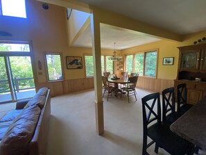 A spacious room with a large dining table, wooden chairs, and a view of trees through large windows.