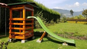 Eine hölzerne Spielkonstruktion mit Rutsche auf einer Wiese, im Hintergrund Berge.