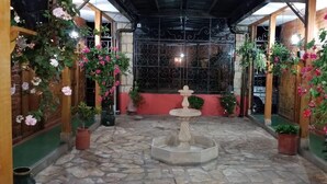 Ein Innenhof mit Steinböden, einer zentralen Fontäne und umgeben von Blumentöpfen und Blumen.