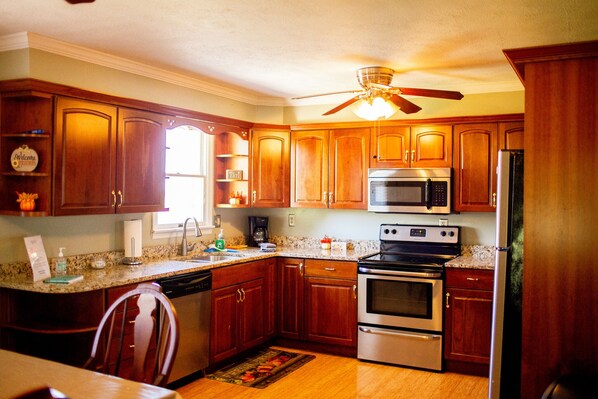 A kitchen with wooden cabinets, stainless steel appliances, a granite countertop, and a ceiling fan.
