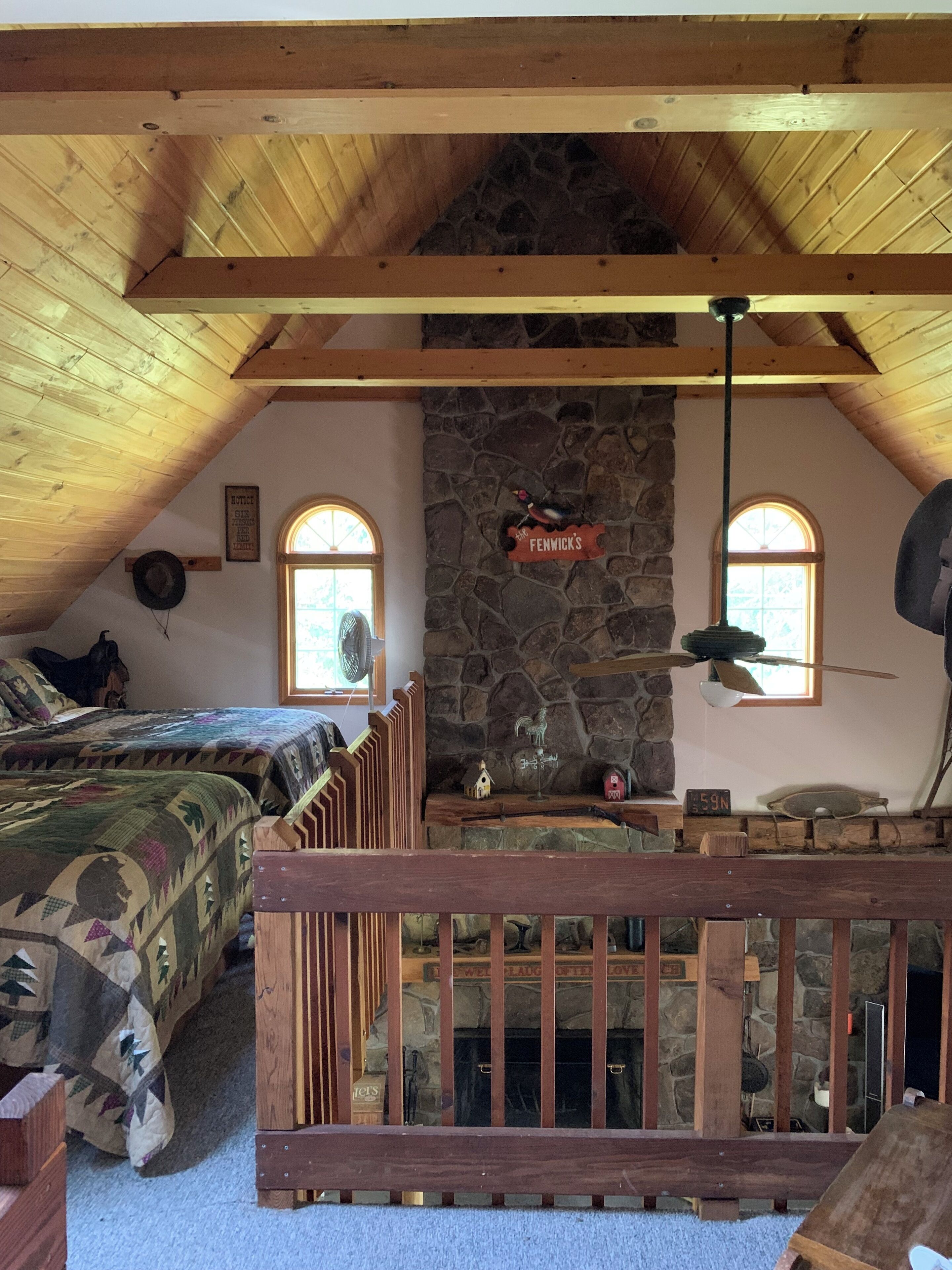 Une chambre mansardée chaleureuse avec un mur en pierre, des poutres en bois, un lit recouvert d’une couette à motifs camouflage, un banc en bois et une cheminée en pierre.