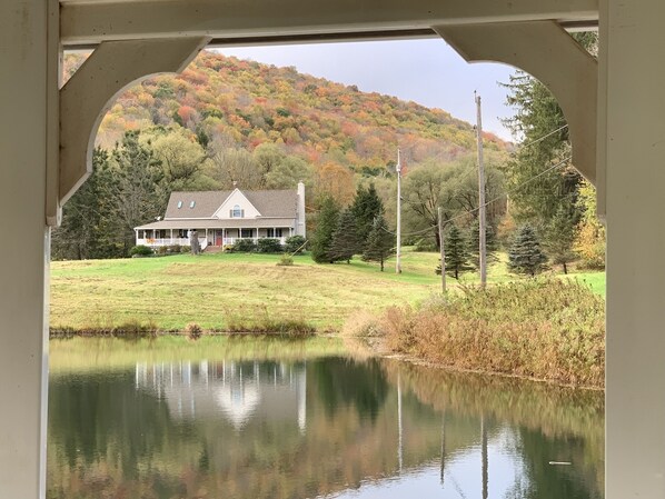 A house with a porch, a pond in the foreground, and a forested hill in the background. - A Rustic Retreat at Wolf Hollow Farm (Andes)