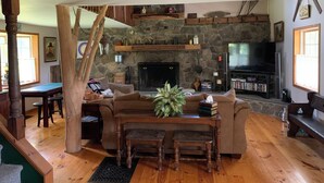 A cozy living room with a stone fireplace, wooden furniture, and a television. - A Rustic Retreat at Wolf Hollow Farm (Andes)