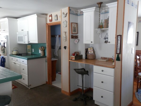A kitchen with white cabinets, a green countertop, and a wooden stool. There is a white door leading to a bathroom. - A Rustic Retreat at Wolf Hollow Farm (Andes)