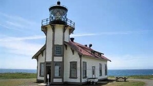Un phare doté d’une tour et d’une base, situé sur une pelouse, avec un banc et une table de pique-nique à proximité.