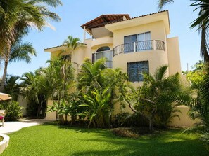 A two-story building with a balcony, surrounded by lush greenery and palm trees.