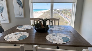 A dining table with a view of the beach, a potted plant, and decorative placemats.