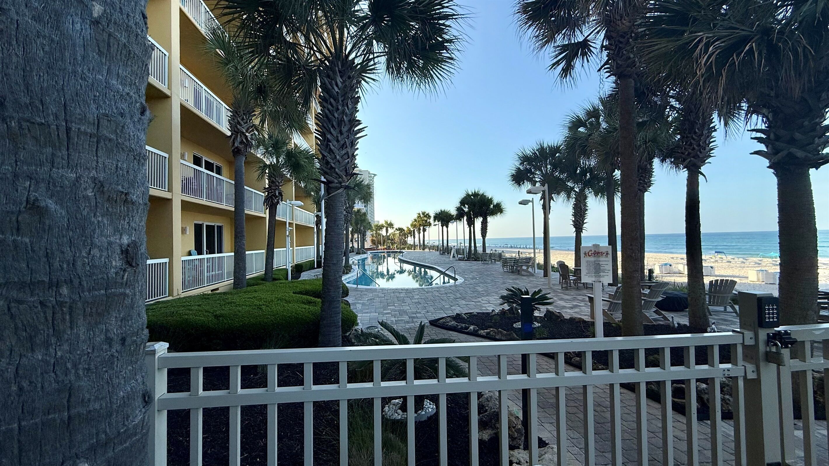 Een resort met een zwembad, palmbomen en uitzicht op het strand.