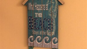 A decorative sign with the text "What Happens at the Beach Stays at the Beach" mounted on a wall. - Walk to everything downtown and beach (Dewey Beach)