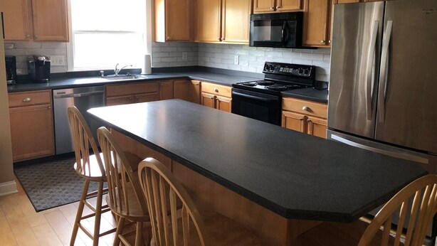A modern kitchen with wooden cabinets, a stainless steel refrigerator, a black stove, and a large island with bar stools. - Walk to everything downtown and beach (Dewey Beach)
