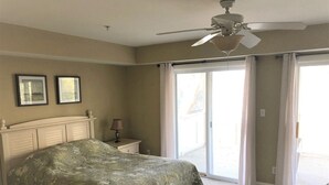 A bedroom with a bed, a nightstand, a lamp, a ceiling fan, and a sliding glass door leading to a balcony. - Walk to everything downtown and beach (Dewey Beach)