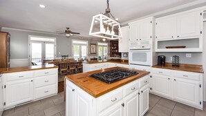 A spacious kitchen with white cabinetry, a central island with a stove, and a ceiling fan. - Oceanfront Home, Stunning Views, Sun Deck, Screened Porch, Walk to restaurants! (Sullivan's Island)