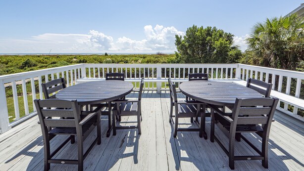 A wooden deck with a table and chairs, overlooking a beach and greenery. - Oceanfront Home, Stunning Views, Sun Deck, Screened Porch, Walk to restaurants! (Sullivan's Island)