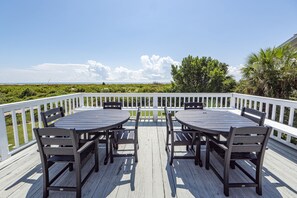 A wooden deck with a table and chairs, overlooking a beach and greenery. - Oceanfront Home, Stunning Views, Sun Deck, Screened Porch, Walk to restaurants! (Sullivan's Island)