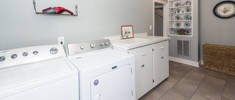 A laundry room with a washer and dryer, a sink, and a shelving unit with decorative plates.
