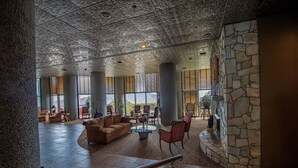 A spacious lobby with a high ceiling, stone columns, and a stone fireplace. There are several seating areas with couches and chairs.