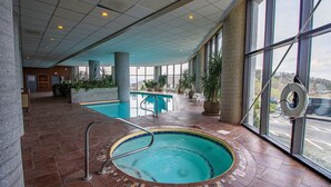 An indoor swimming pool with a tiled floor, a metal ladder, and large windows offering a view of the outside.