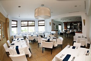 A spacious dining area with multiple tables set for dining, large windows allowing natural light, and a view of the kitchen area in the background. - Amazing WATERVIEW in every room, 16 floor, PORTOFINO - oceanfront resort  (Gulf Breeze)