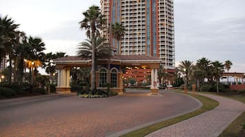 A hotel entrance with a curved brick pathway, palm trees, and a large building with multiple floors and balconies.