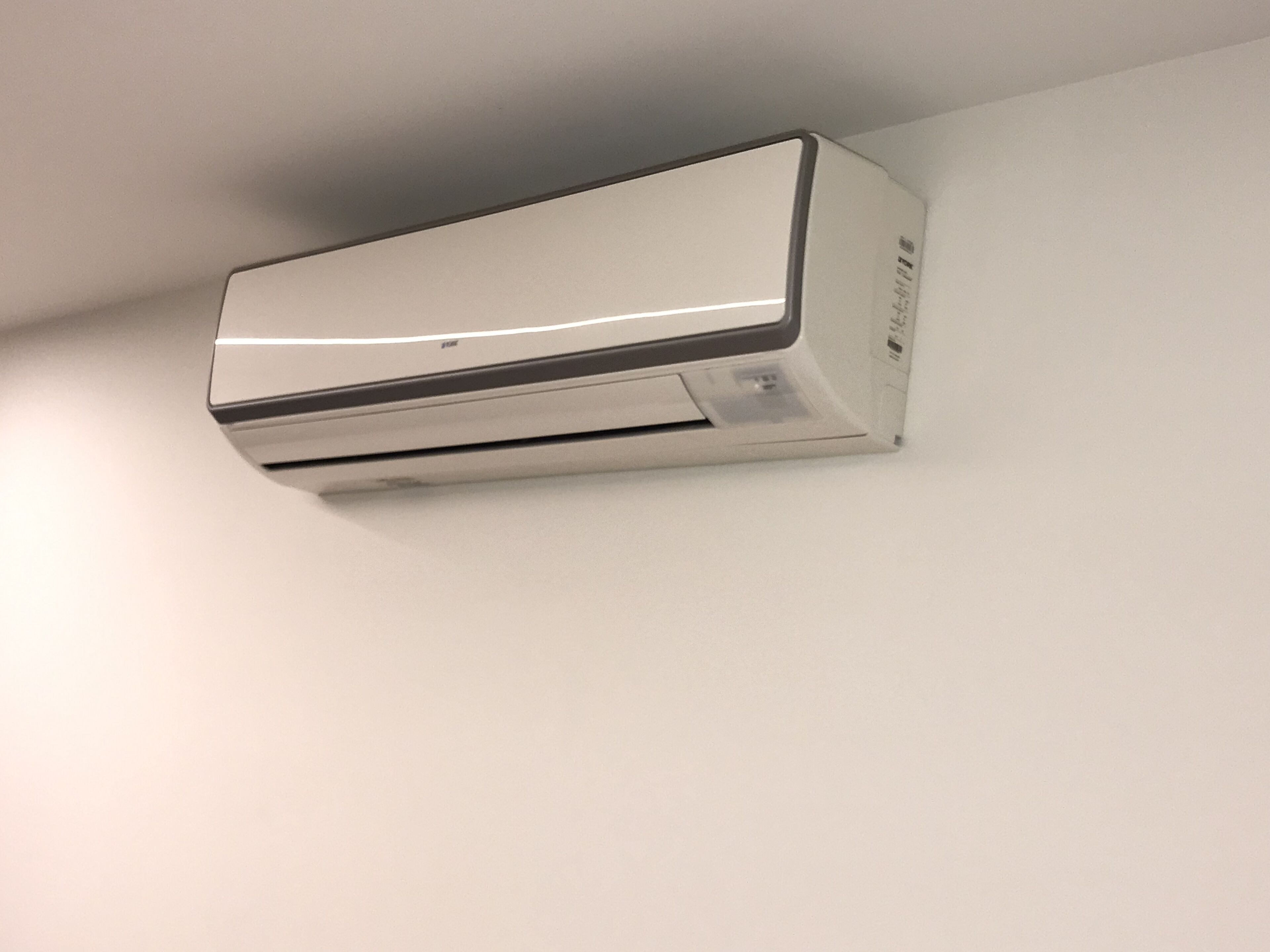 Ar condicionado moderno fixado na parede, num quarto com paredes brancas.
