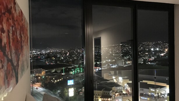 A bedroom with a large window overlooking a cityscape at night.