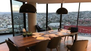 A modern dining area with a panoramic city view, a wooden table, and several chairs.