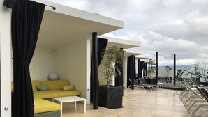 A modern outdoor seating area with a yellow sofa, a white table, and black curtains.