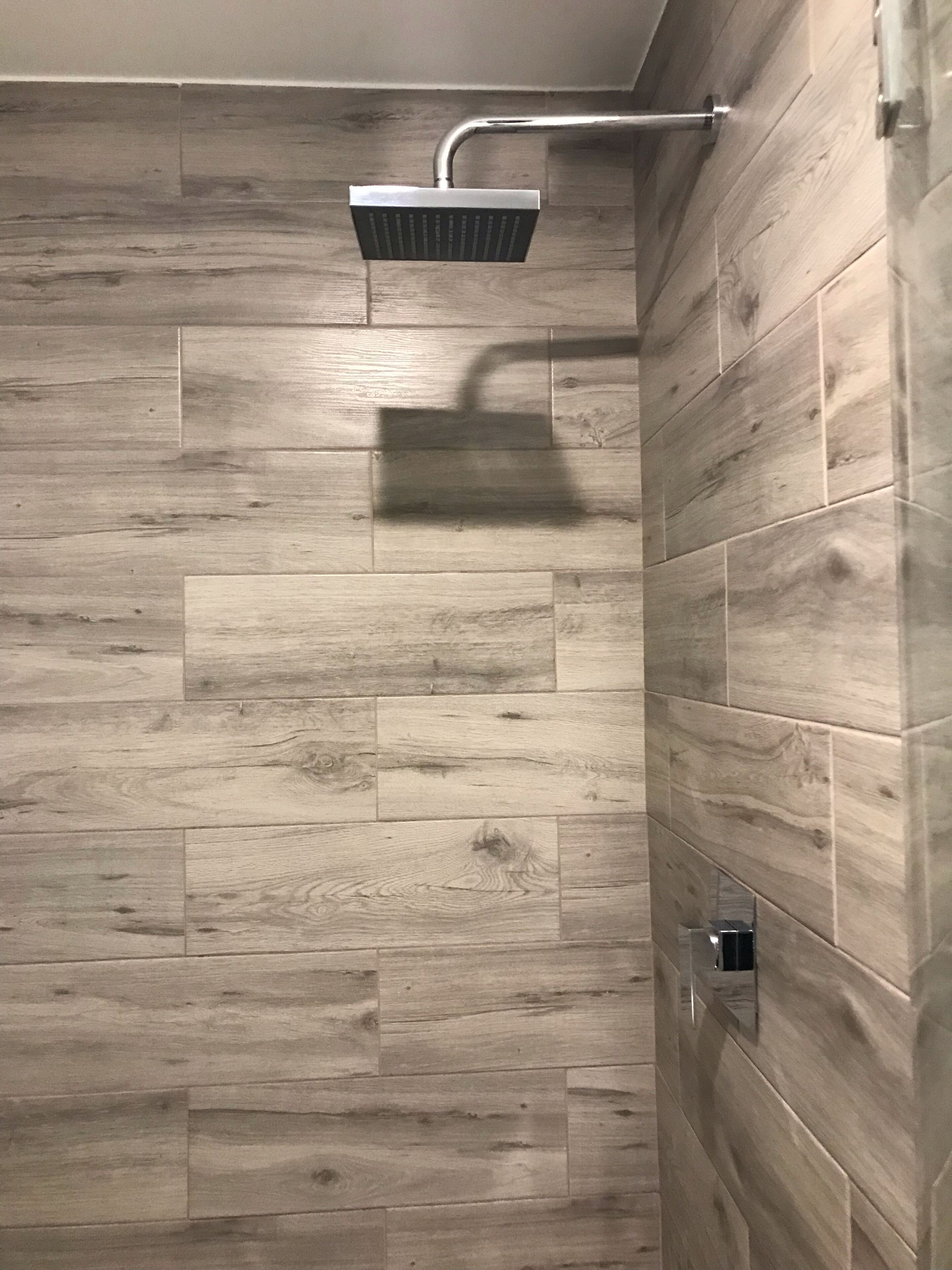 Ducha de diseño moderno, con panel de pared de madera y cabezal de ducha cromado.