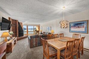 A spacious living area with a fireplace, a large window, a dining table with chairs, and a mounted TV. - Dillon Lake 2 BR Condo-Pool, Hot Tub, 4 lift passes at Keystone-Breck & Arapahoe (Dillon)