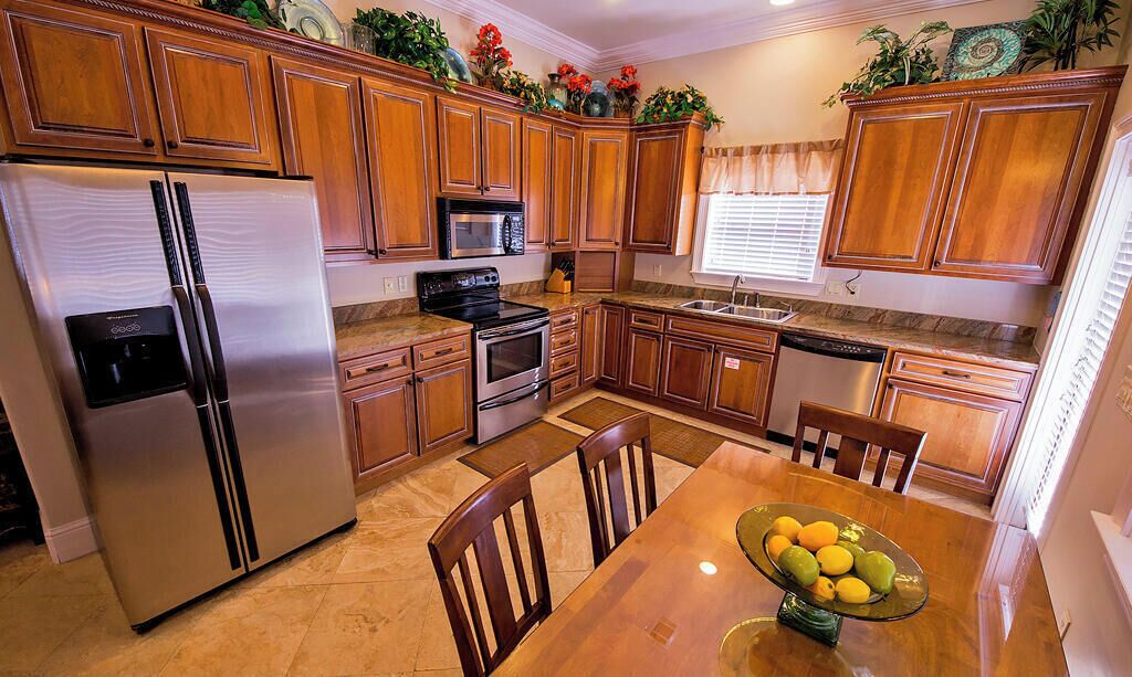 A kitchen with wooden cabinets, stainless steel appliances, a dining table with chairs, and a bowl of fruit.