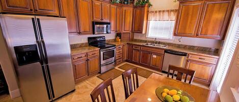 A kitchen with wooden cabinets, stainless steel appliances, a dining table with chairs, and a bowl of fruit.