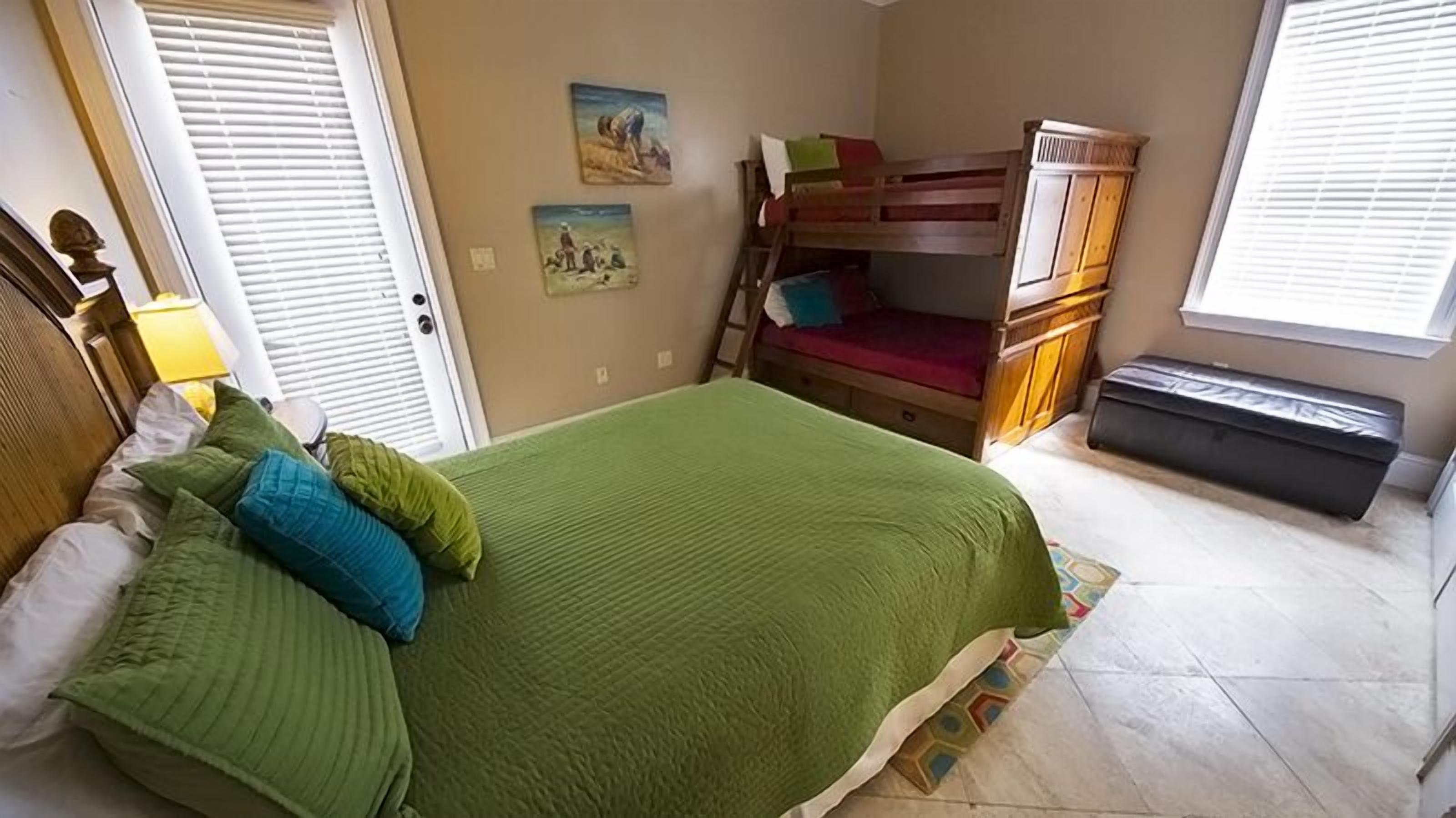 A bedroom with a bunk bed, a green bedspread, and a window with blinds.