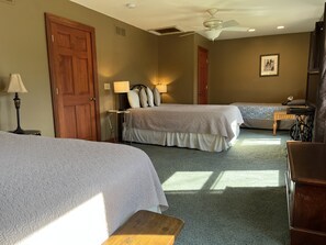 Une chambre d’hôtel avec deux lits, un ventilateur de plafond, un bureau avec une chaise et une lampe.