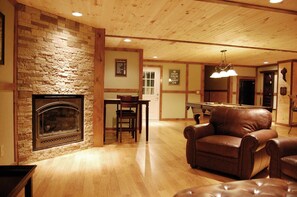 A cozy living room with a stone fireplace, wooden ceiling, and a pool table.