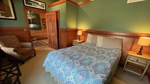 Ein Schlafzimmer mit einem großen Bett, einem Sessel, einem Nachttisch mit Lampe und einer Tür.