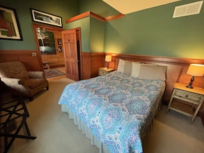 A bedroom with a large bed, a chair, a nightstand with a lamp, and a door. - Harvest Moon Lodge at Harvest Moon Cottages, LLC (Rockbridge)