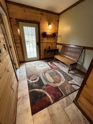 Interior de madera con un banco, una alfombra y una puerta que da al exterior.