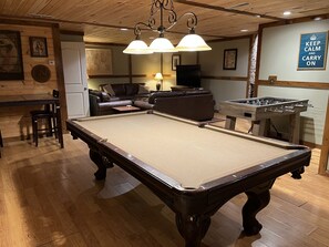 Une table de billard dans une pièce dont le sol est en bois, avec un canapé et une table de baby-foot.