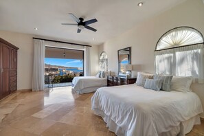 A hotel room with two beds, a balcony, a ceiling fan, and a view of the city.