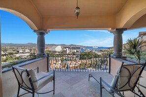 En balkon med to stole, udsigt til en lystbådehavn og et bjergrigt landskab.