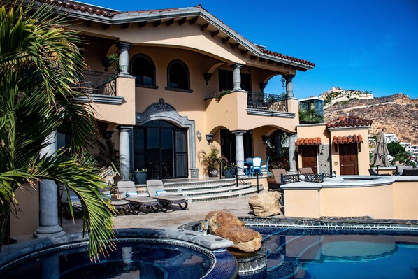 A Mediterranean-style building with a swimming pool, outdoor seating, and a mountainous backdrop.