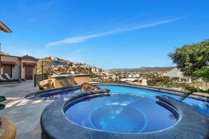 A swimming pool with a hot tub, lounge chairs, and a view of a hillside town.