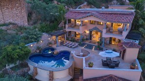 A multi-story house with a swimming pool, outdoor seating, and a patio area.