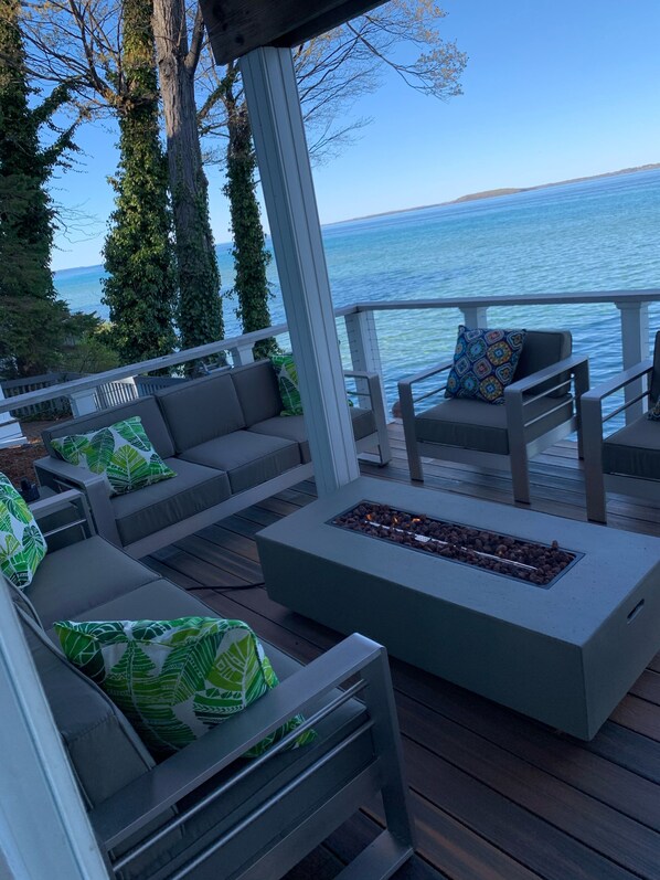 A deck with outdoor seating, a fire pit, and a view of the water. - Beautiful Large House On Water Just 5 Miles To TC (Traverse City)